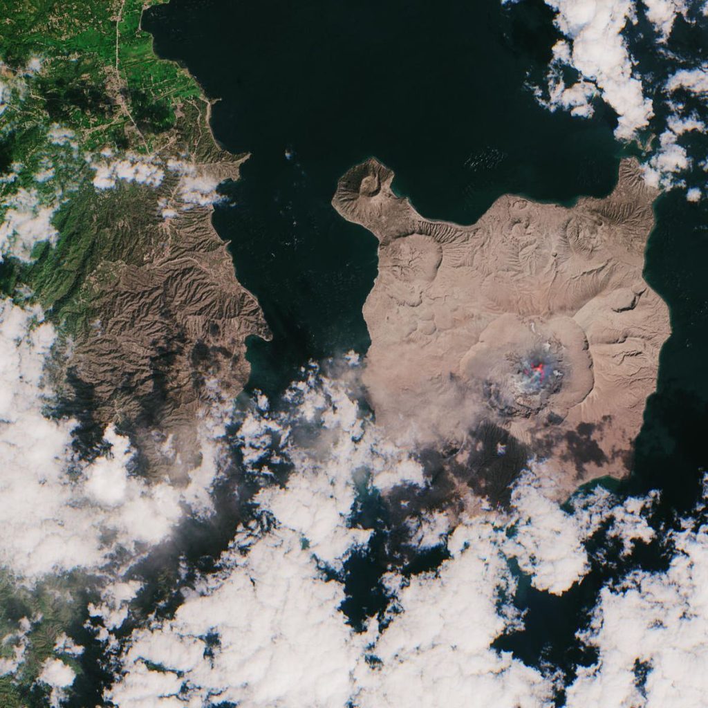 Island Volcano Ash Plume Reshapes Local Air Routes A volcanic eruption on an island sending a thick grey ash cloud into the sky above the coast.