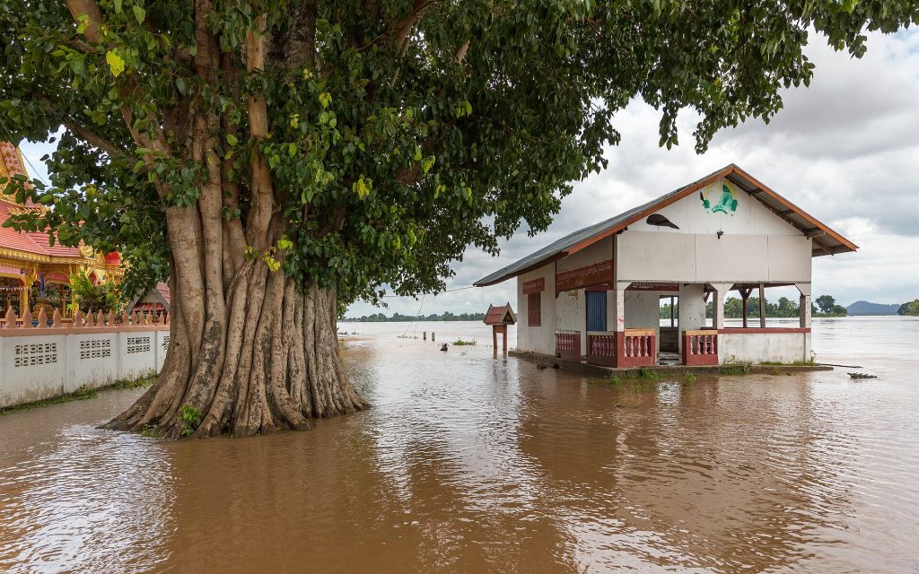Climate Risk Is Rewriting the Price of Home Insurance A building surrounded by muddy floodwater and trees